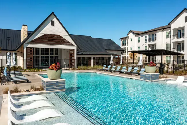 A large swimming pool surrounded by chairs and a fence at Atlas Bluewood in Celina, TX.