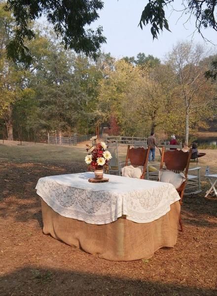 Round outdoor table with white lace cloth and floral centerpiece in a wooded garden setting