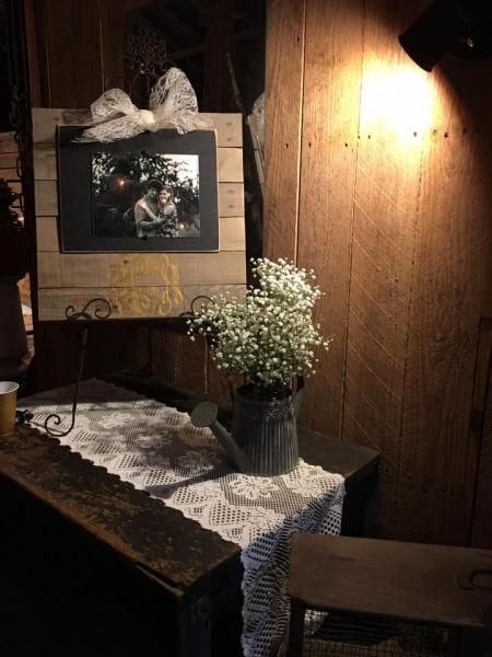 Rustic wooden desk with lace runner, flowers in vase, framed art, and warm wall lamp