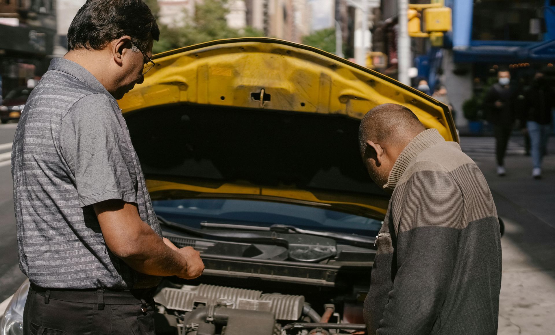 Two men are looking under the hood of a car.