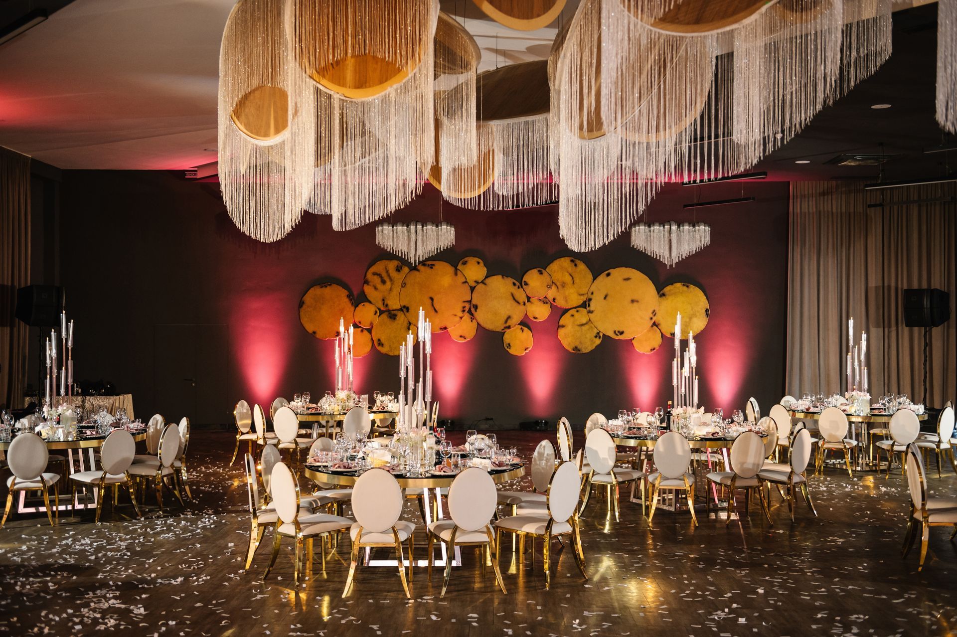 Elegant banquet hall with decorated tables, golden chairs, and glowing ceiling decorations.