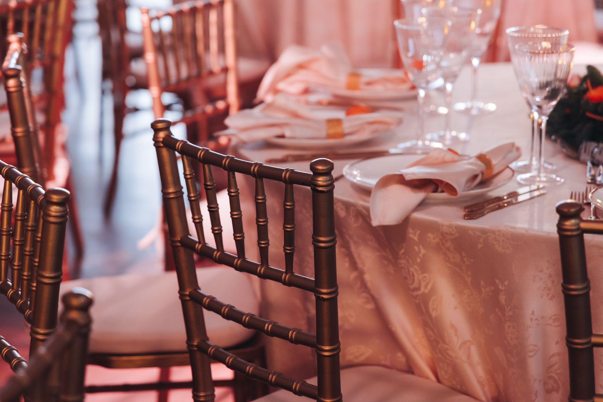 Gold chairs around a table set with plates, glasses, and napkins, in a room with warm lighting.