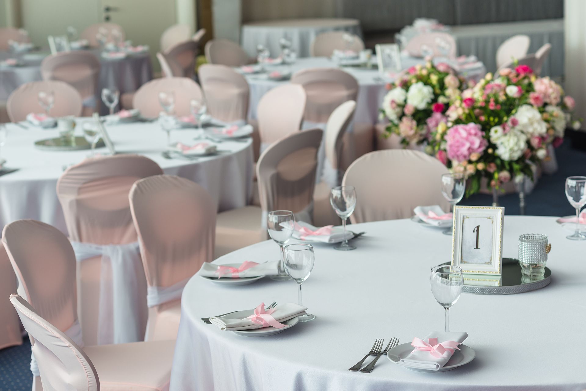 Wedding reception tables with white tablecloths, pink chair covers, floral centerpieces.