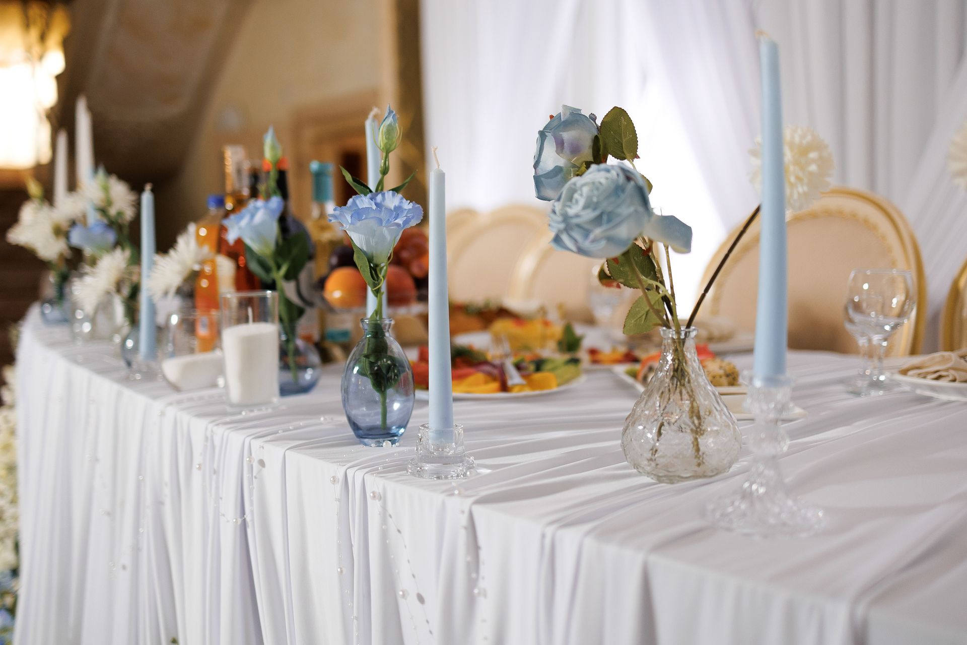 Long table set with blue floral decorations and candles for a celebration.