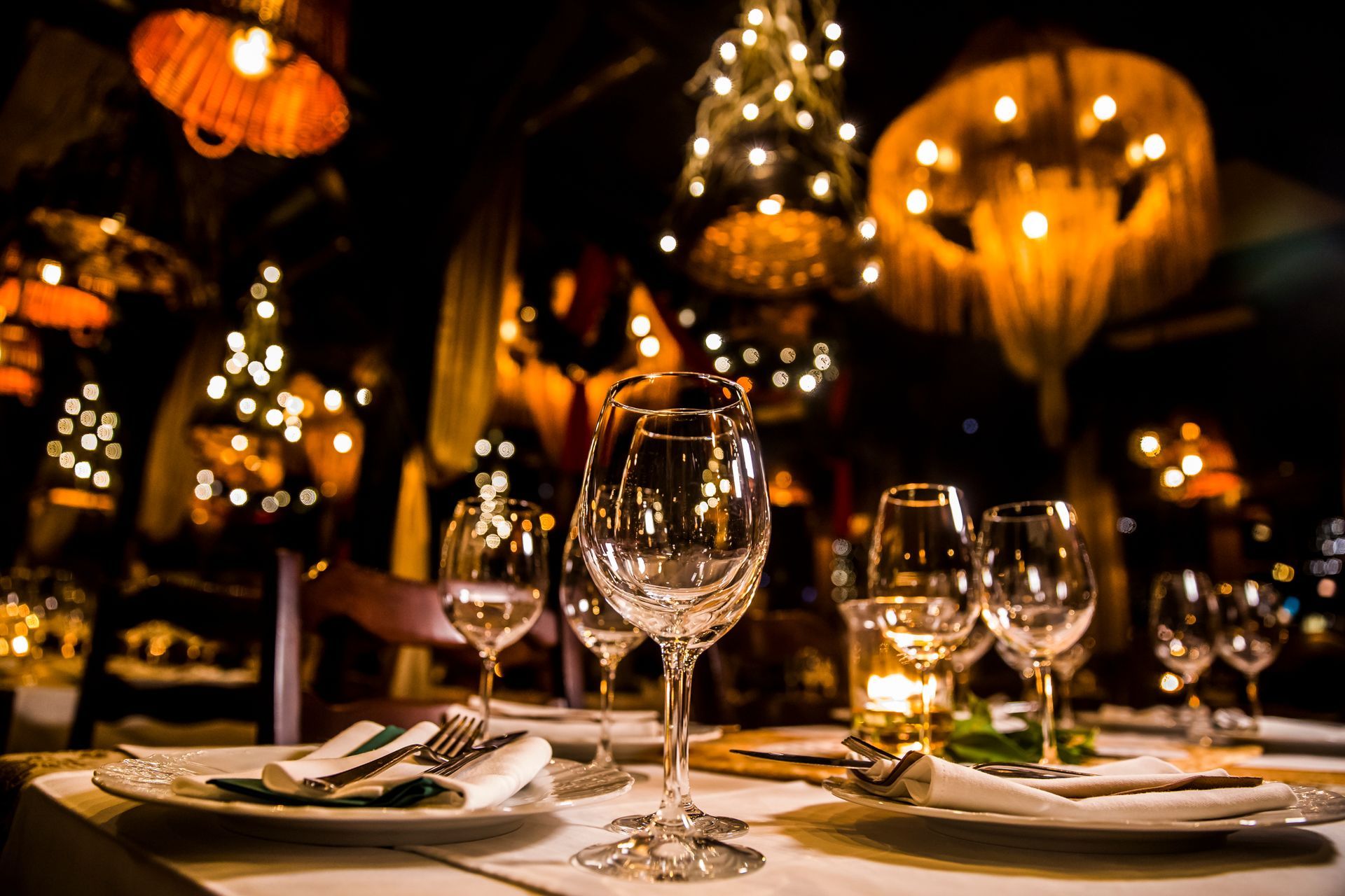Elegant restaurant table setting with wine glasses, lit by warm lights.
