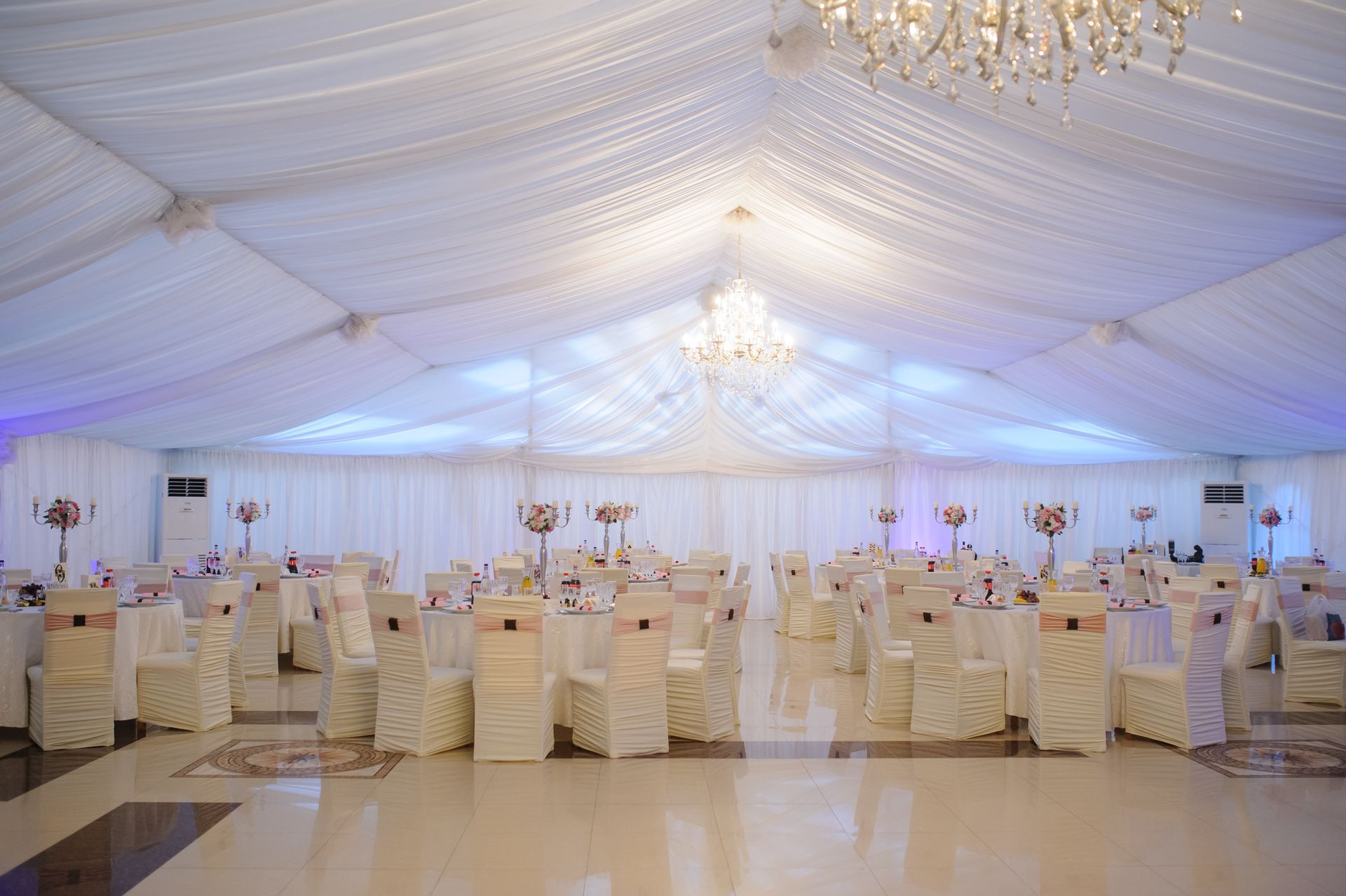 Formal event space with white draping, tables set for guests, and chandeliers.