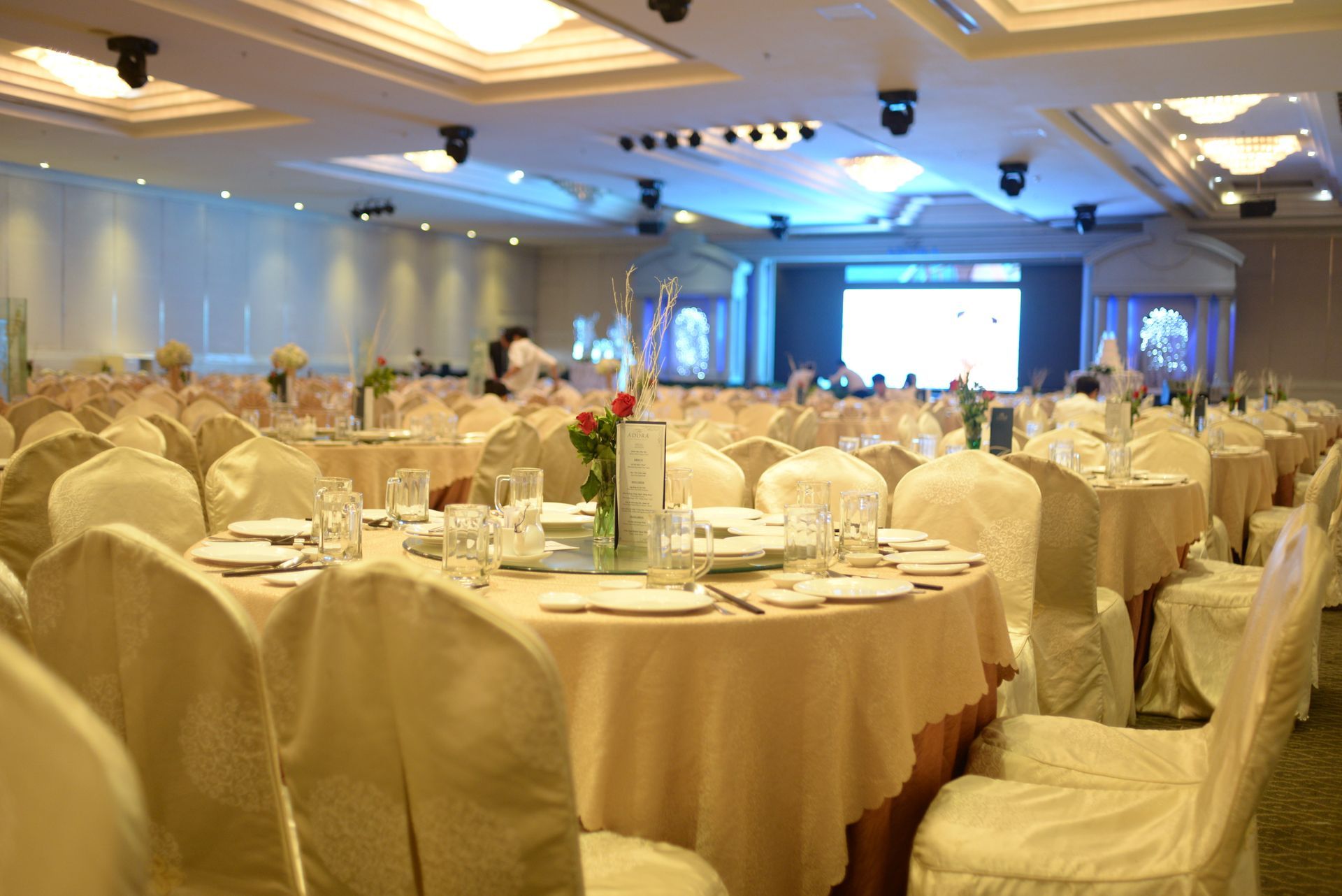 Banquet hall set for a formal event, round tables with beige linens, white-covered chairs.