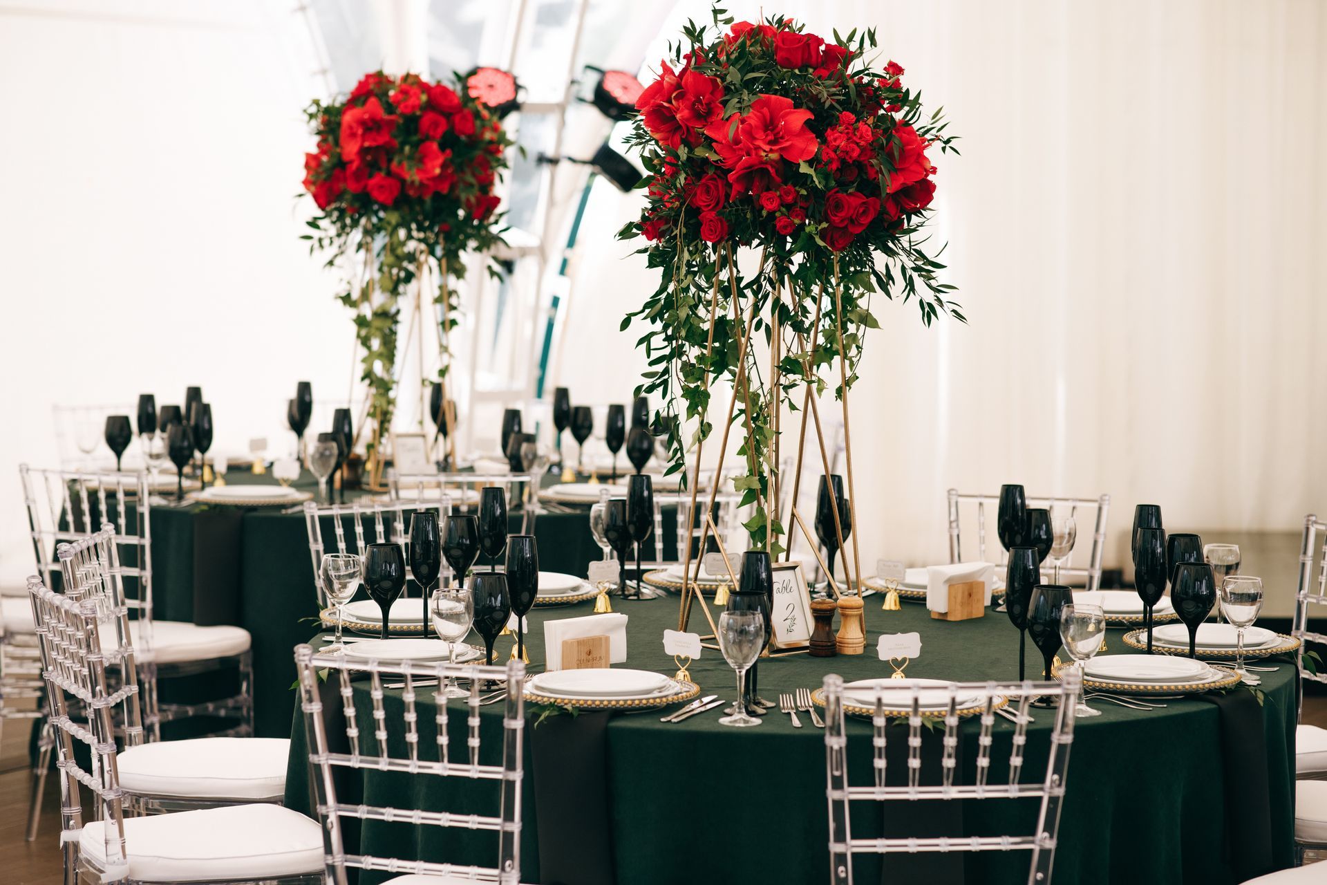 Elegant wedding reception tables with tall red floral centerpieces, dark green linens, and black glassware.