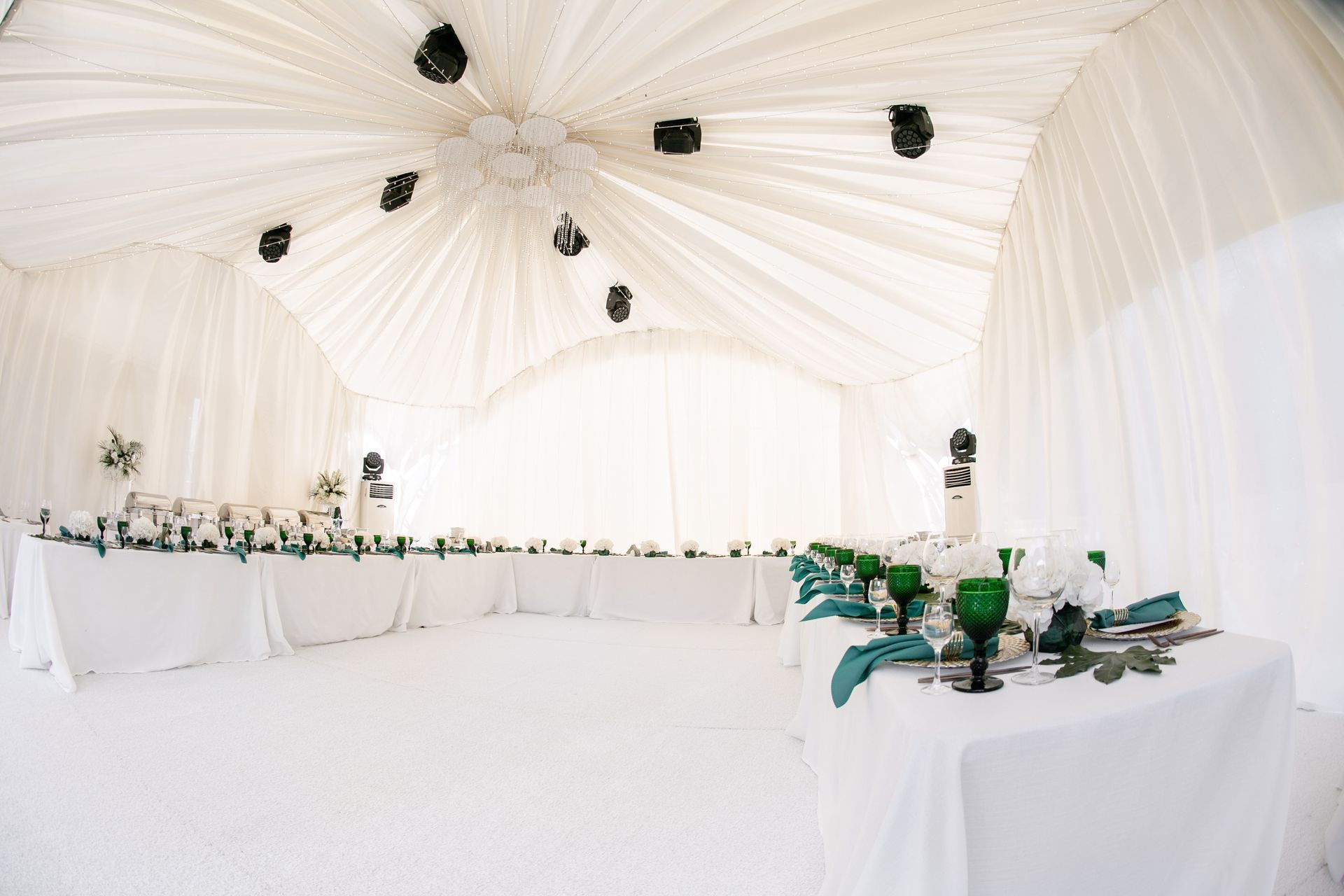 White tent interior, long tables set for a formal event with white linens, flowers, and teal accents.
