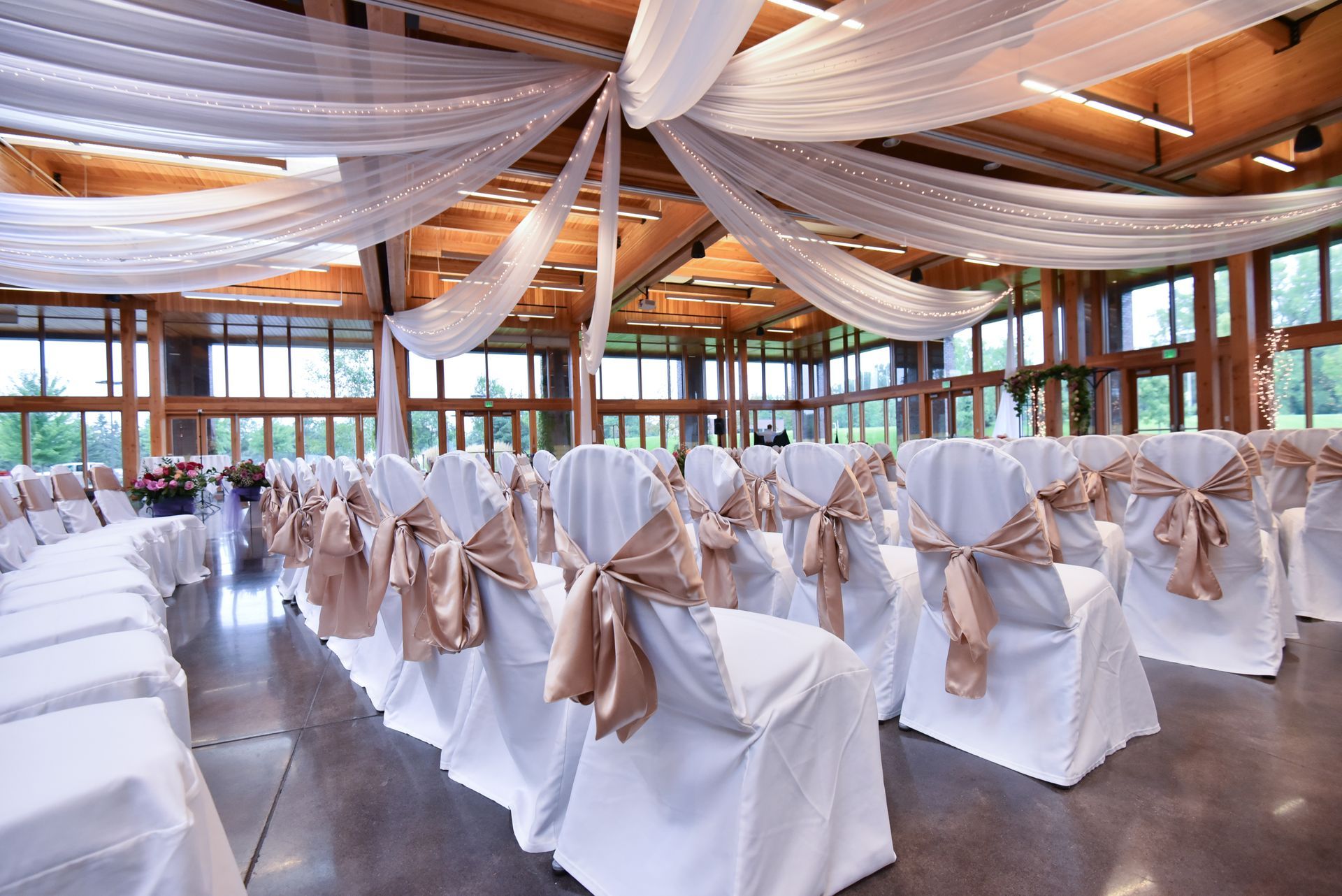 Wedding venue with white draped ceiling and rows of chairs decorated with gold bows.