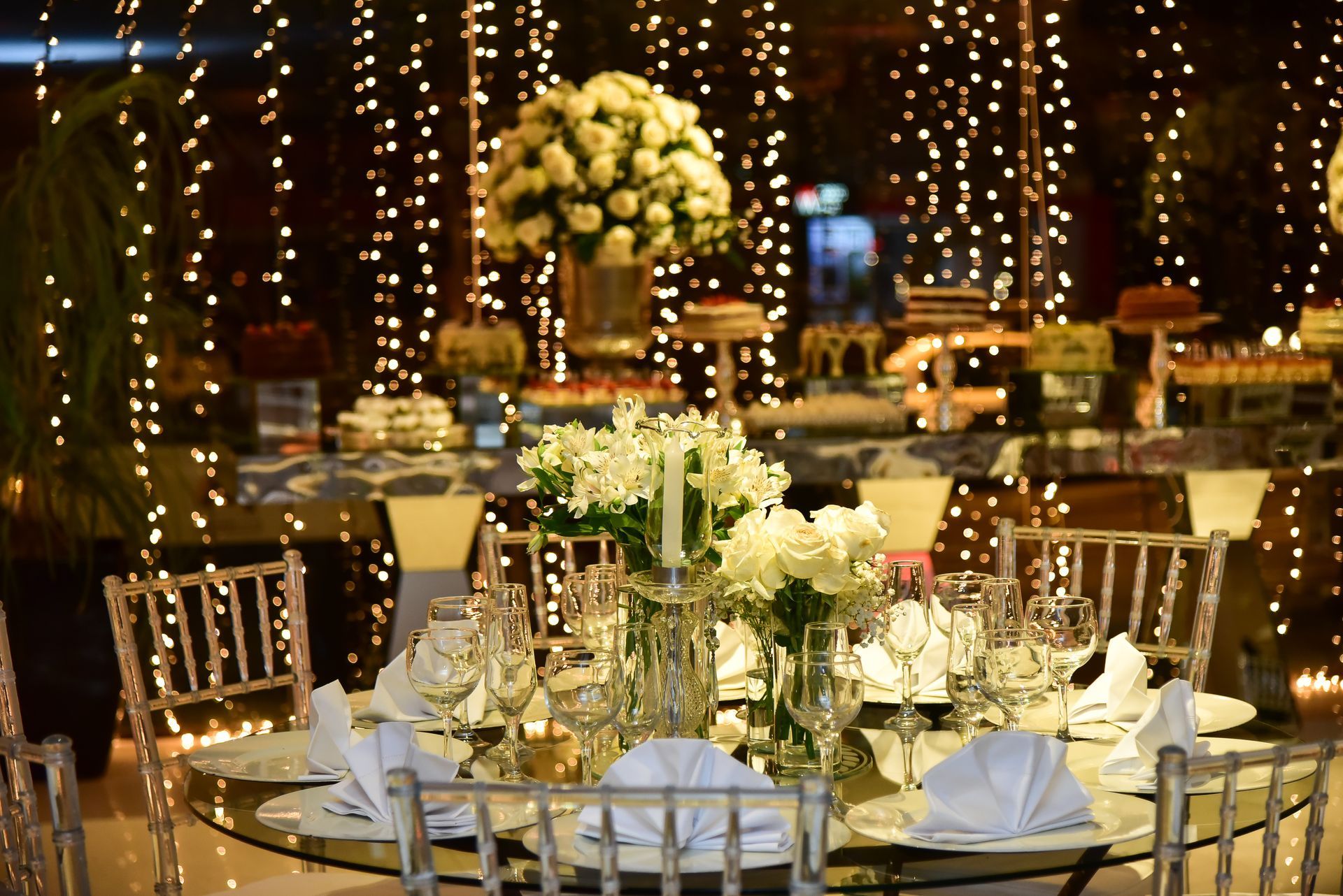 Elegant table setting with white flowers, and fairy lights, with a buffet table in the background.