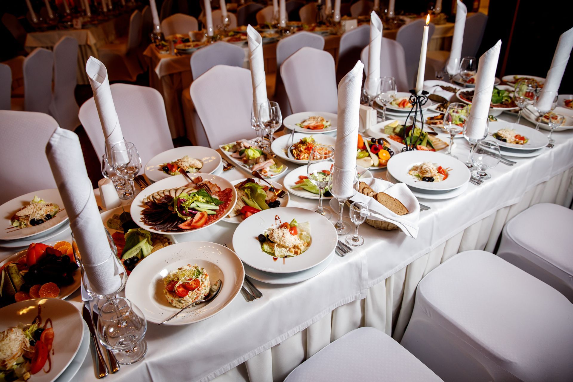 Banquet table set with multiple dishes, white tablecloth, napkins, and candles.