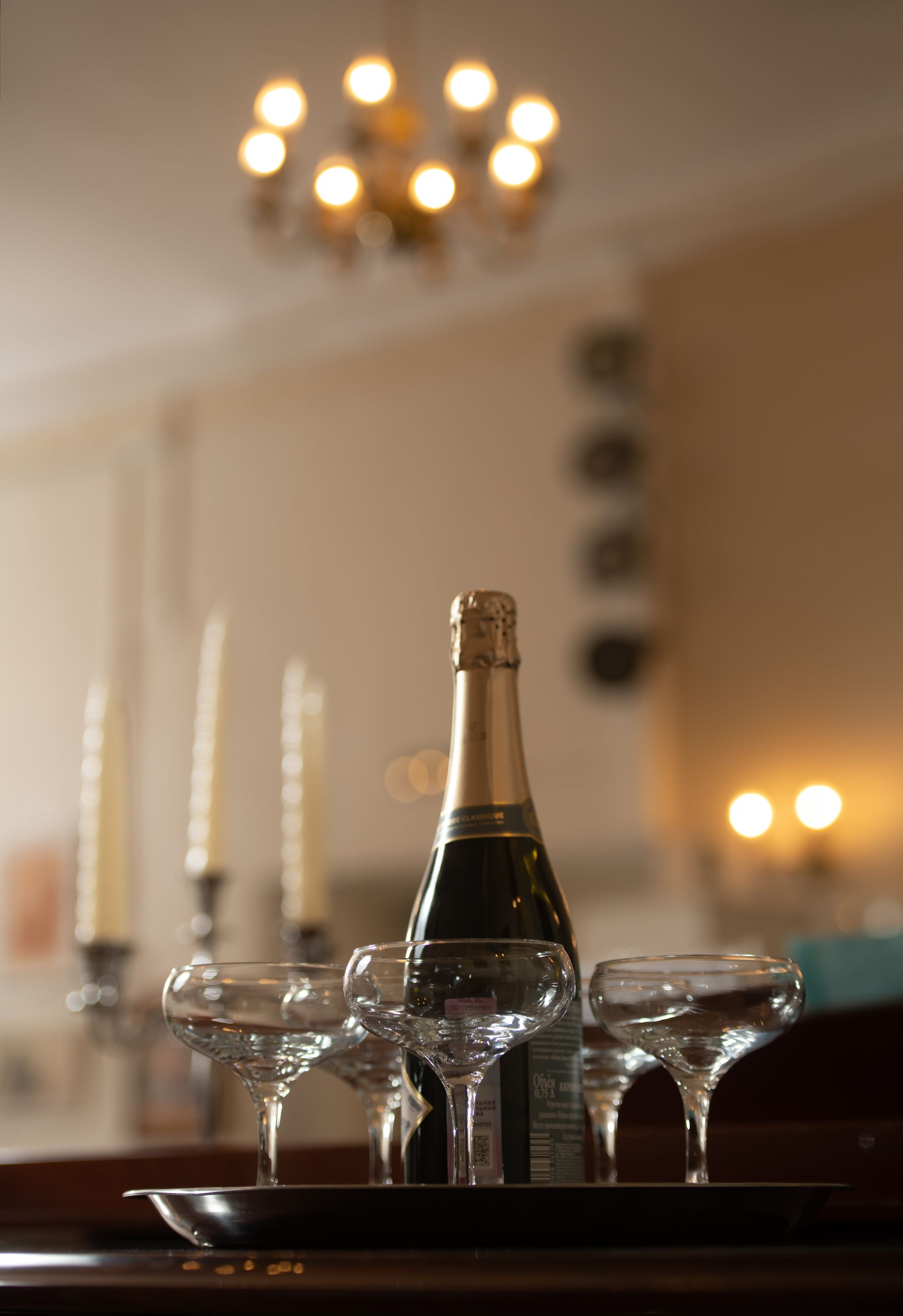 Champagne bottle and glasses on a tray, with candles and a chandelier in the background.