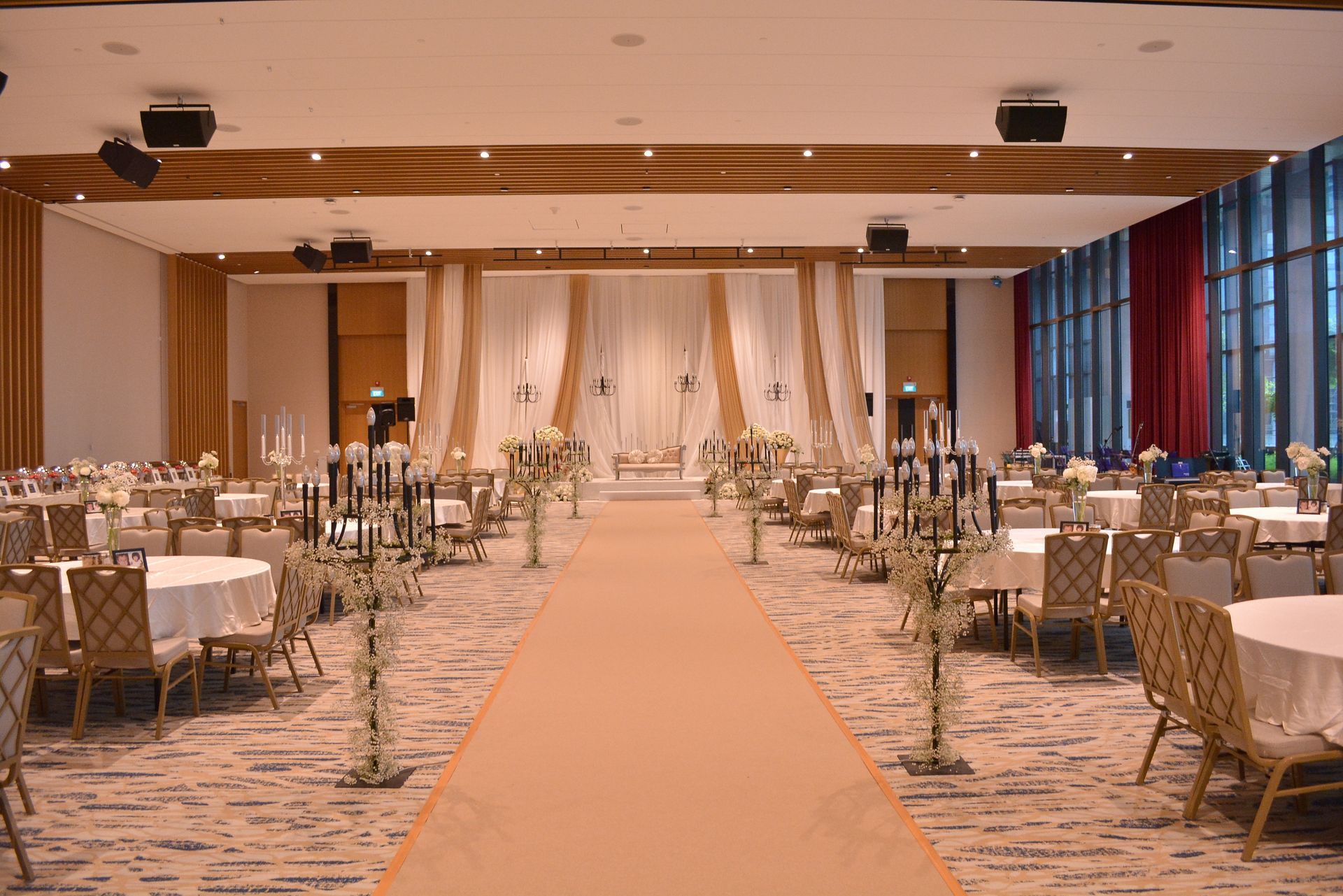 Wedding reception hall with tables, a stage, and a center aisle with floral arrangements.