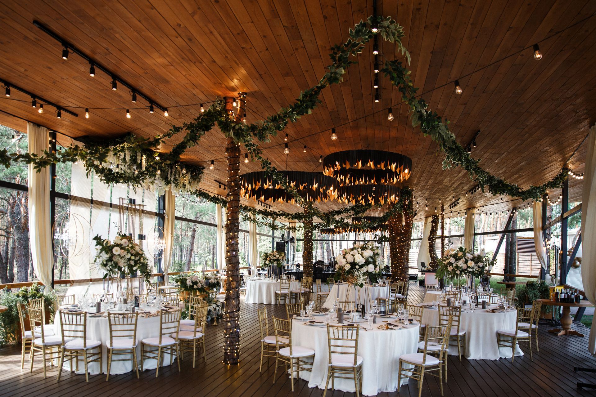 Wedding reception hall with tables, white linens, gold chairs, and floral arrangements.