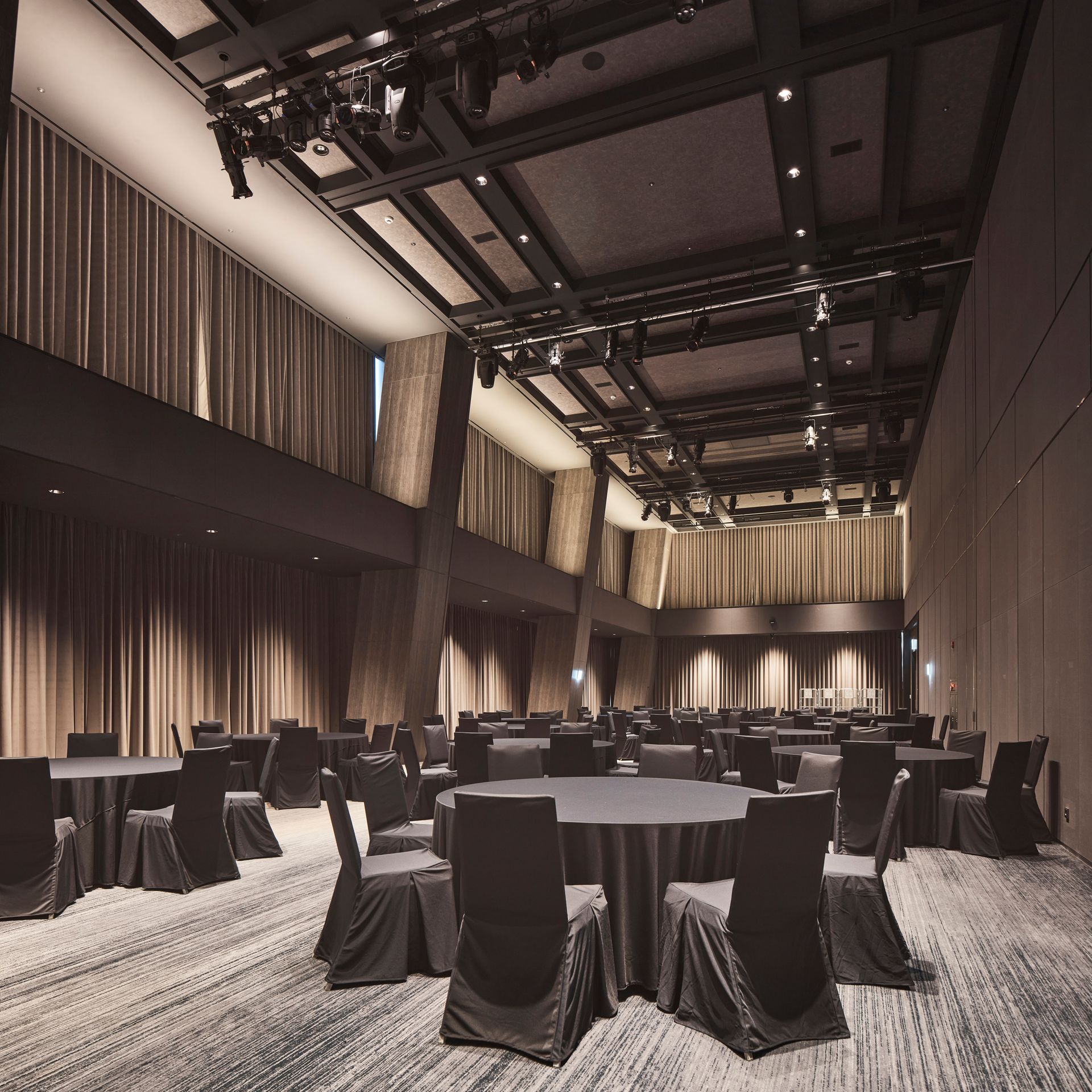 Banquet hall with round tables, chairs, and dark curtains. Black and gray color scheme.