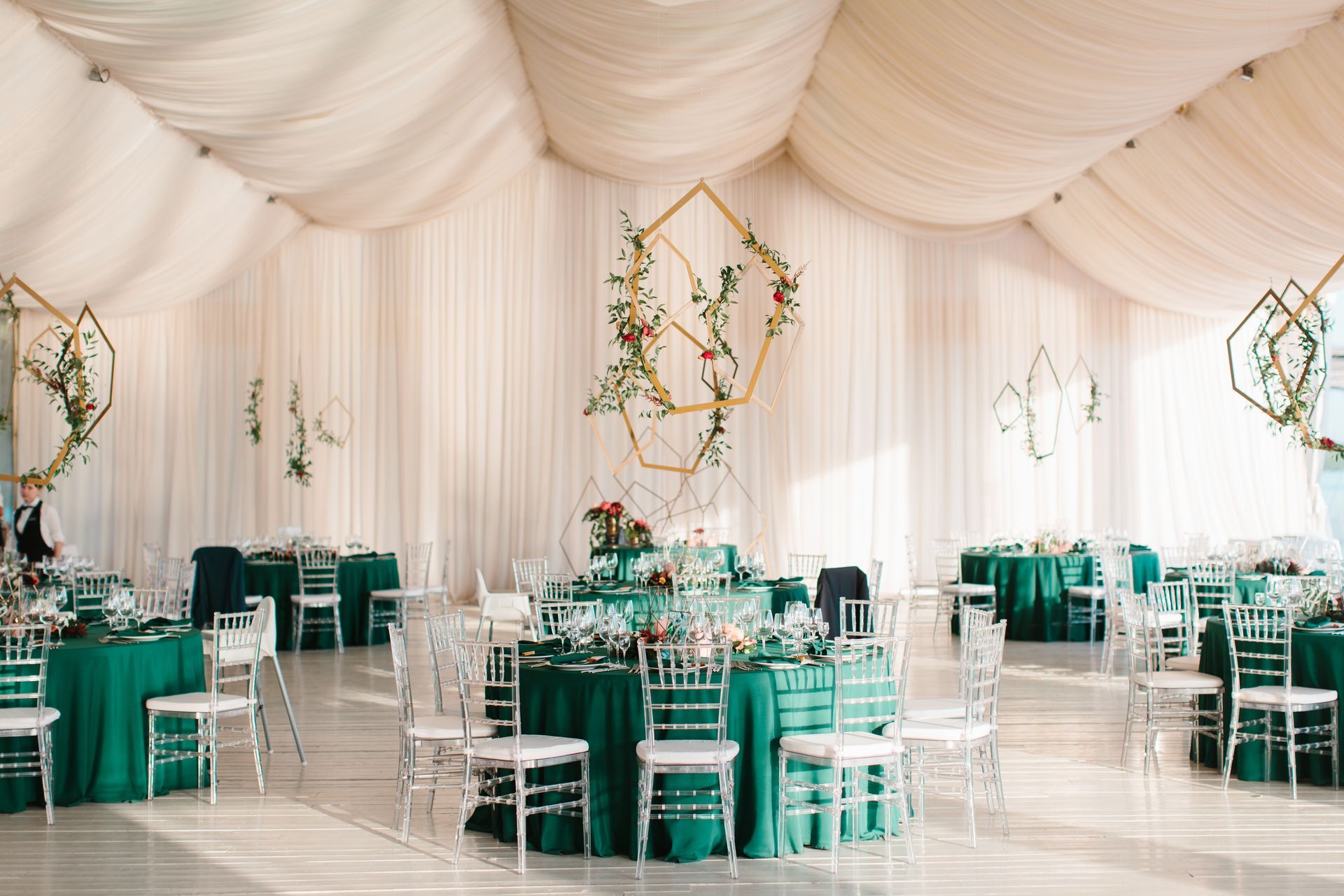 Elegant reception hall with emerald green tablecloths, floral centerpieces, and geometric gold decor.