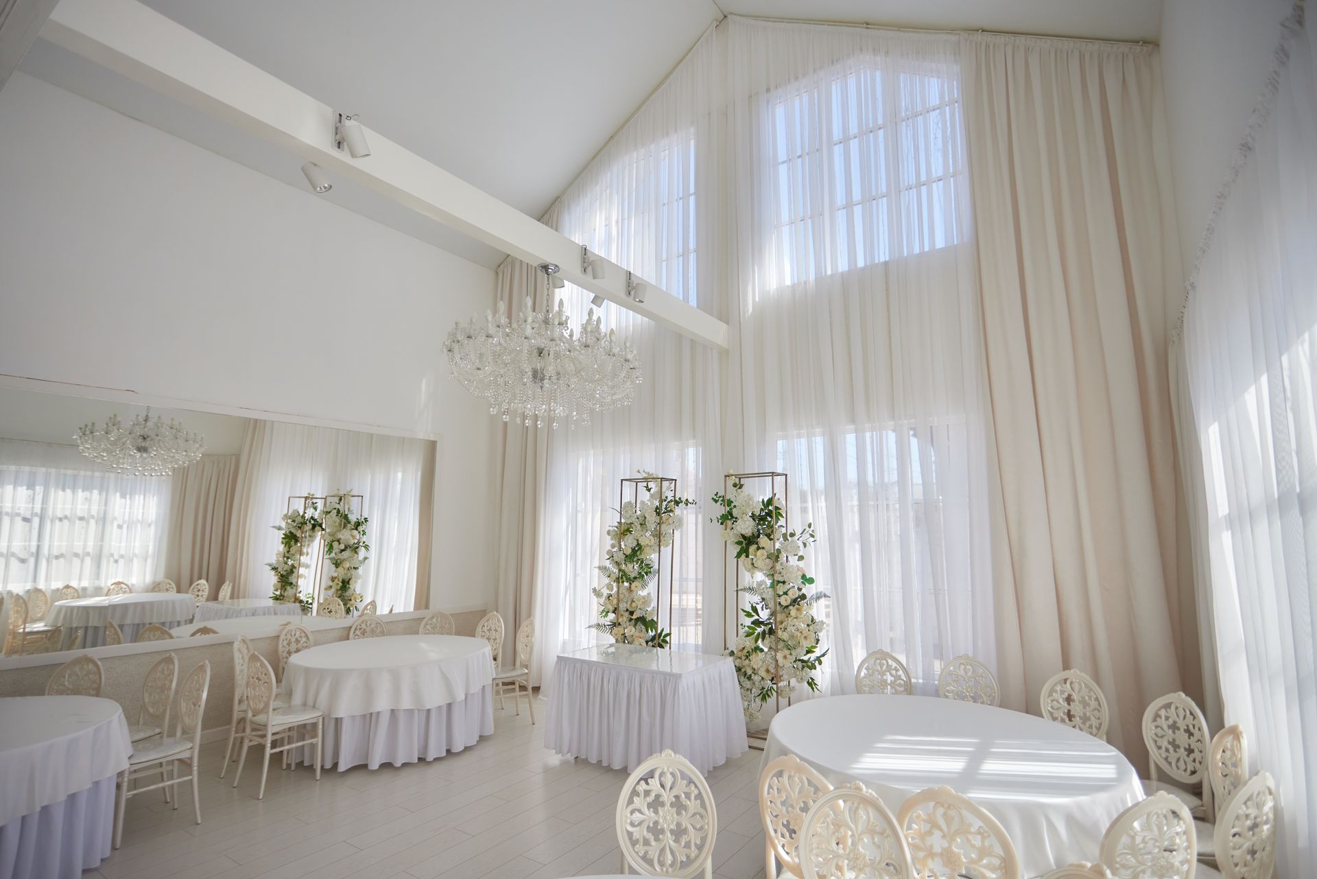 Elegant white wedding reception hall with tables, chairs, and floral decorations.
