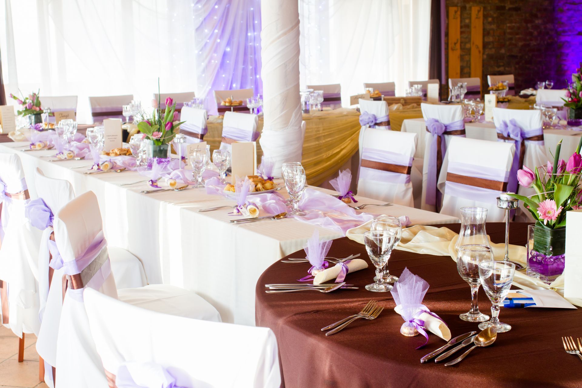 Reception hall decorated for an event with white chairs, brown table cloths, and purple accents.