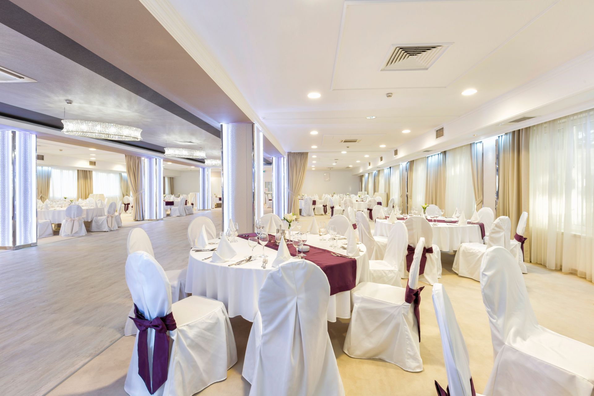 Formal dining hall set for an event with white tablecloths, chairs, and burgundy accents.