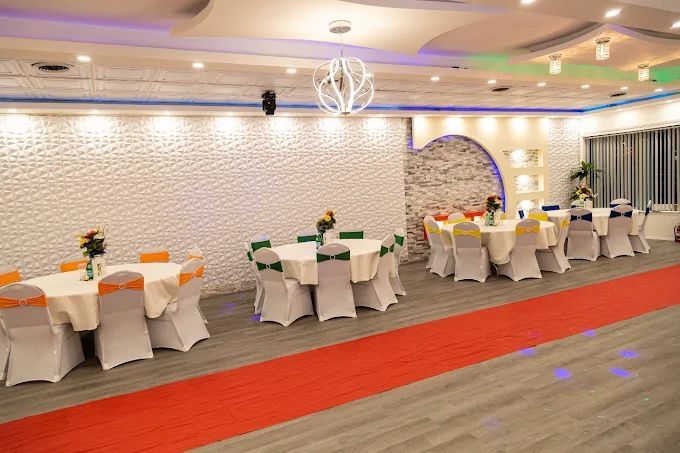 Banquet hall with round tables set for a celebration, white chairs with colorful chair covers, and a red carpet.