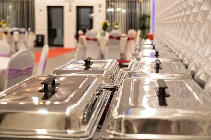 Buffet serving trays in a brightly lit banquet hall.