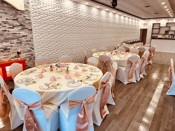 Banquet hall with round tables set for a party, cream table cloths, peach chair sashes, and light-colored walls.