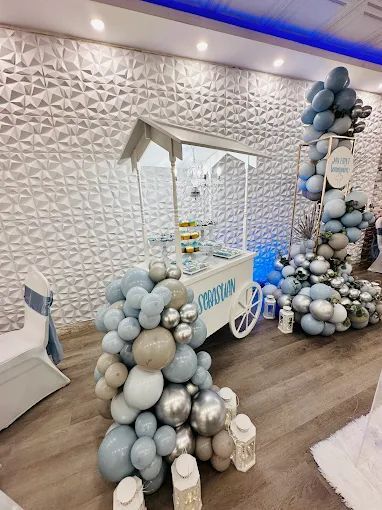A decorated white cart with balloons in a room. Event decor with blue, silver, and tan balloons.
