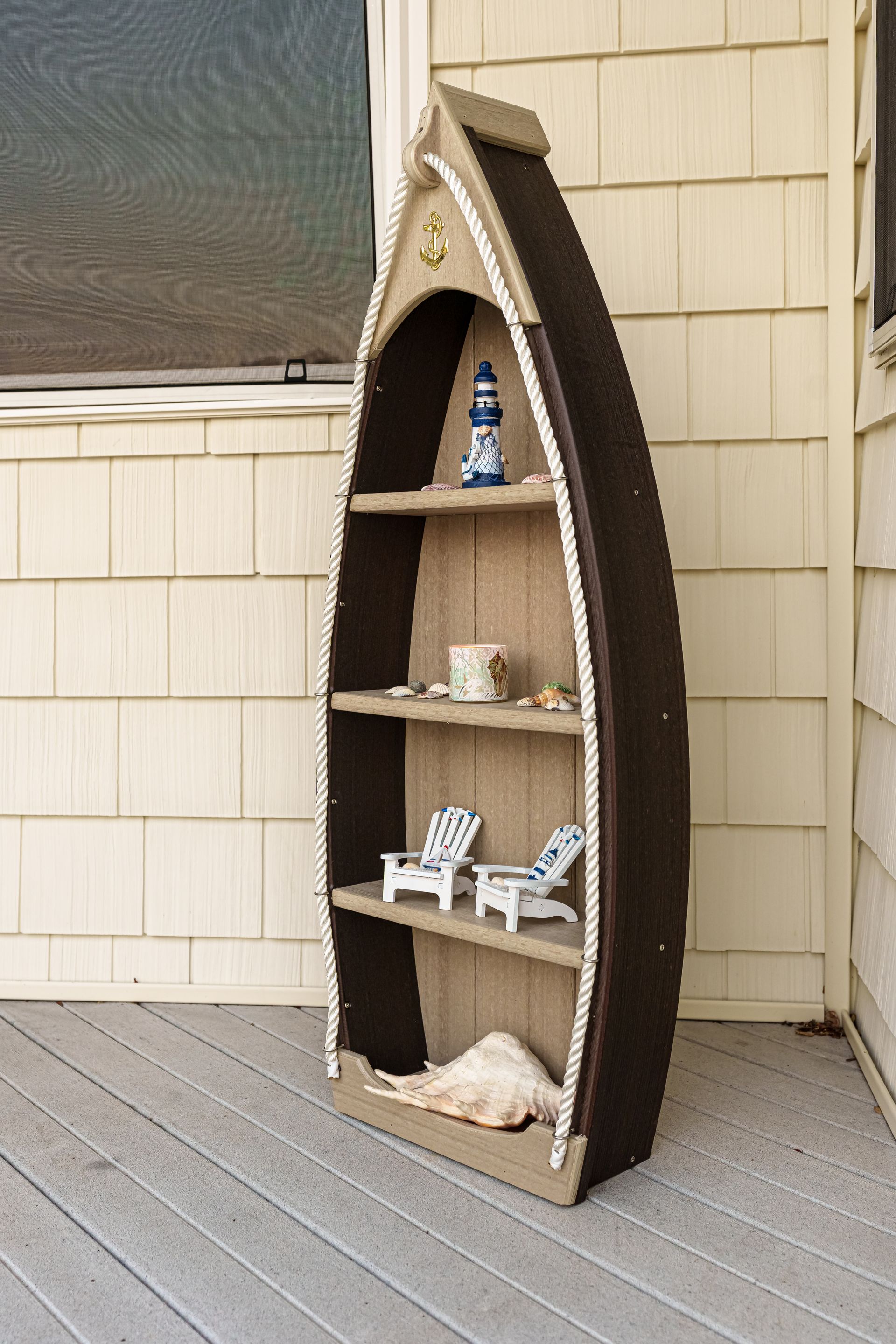Boat-shaped shelf with nautical decor, including a lighthouse, teacup, and seashells, on a wooden deck.