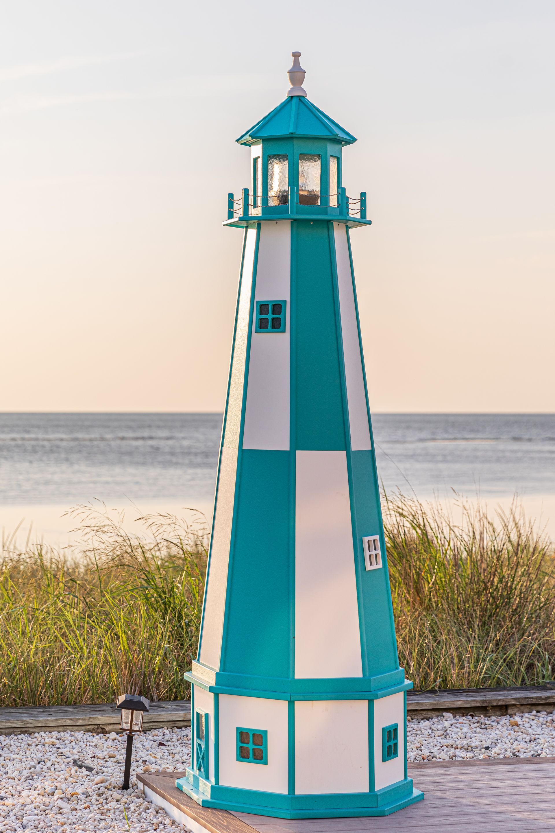 Turquoise and white lighthouse on a brick base, near water and tall grass.