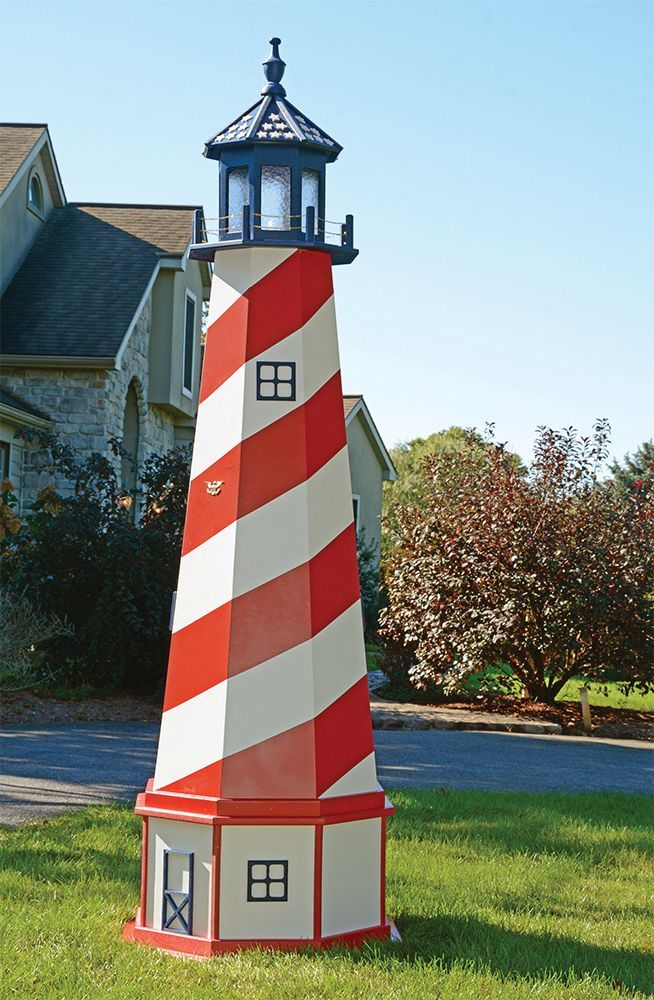 A lawn-ornament lighthouse with red and white diagonal stripes stands in a grassy front yard near a house.