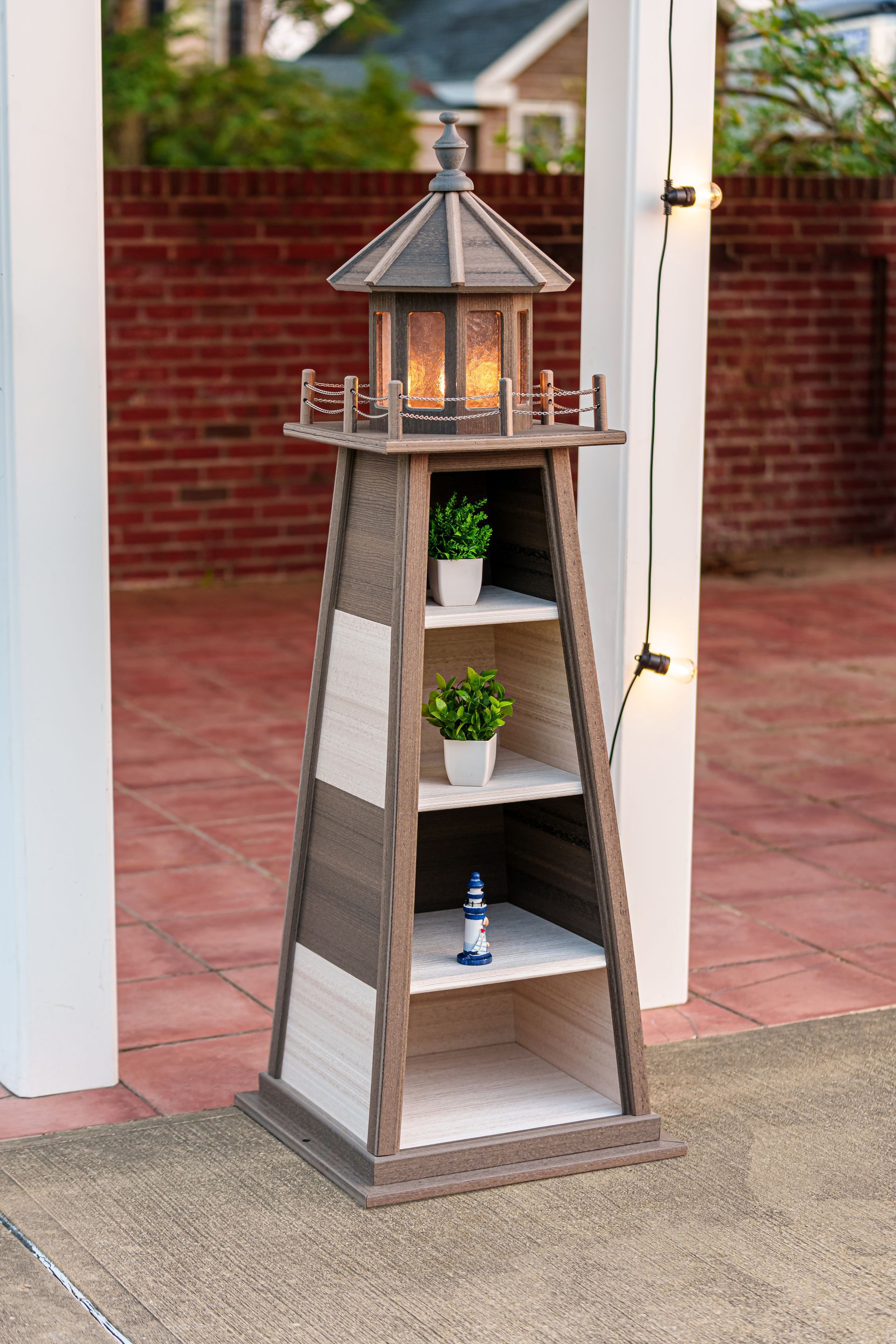 Lighthouse-shaped shelf with lit lantern, potted plants, and small lighthouse figurine on shelves; patio setting.