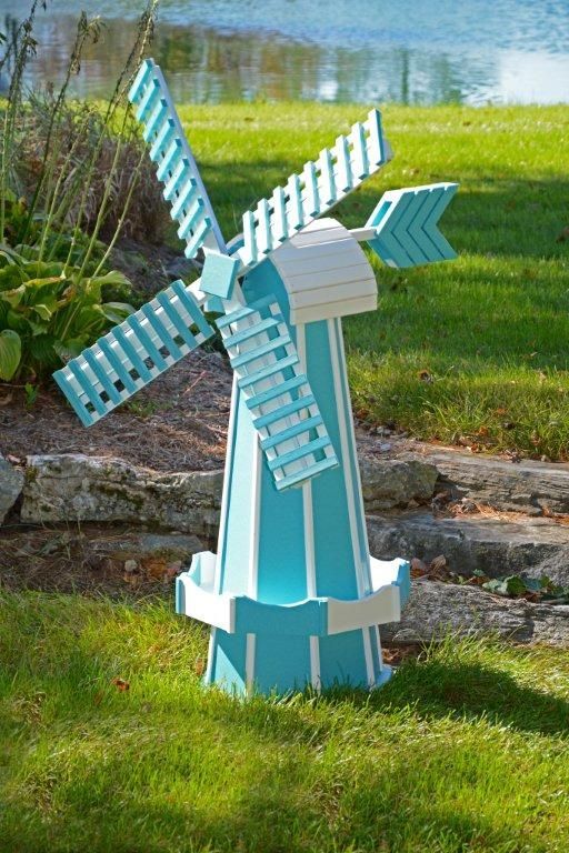 Blue and white wooden windmill in a grassy yard, near a lake.