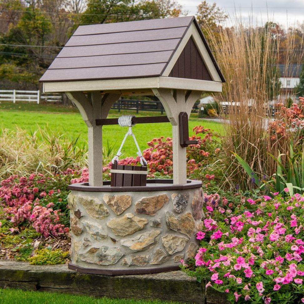 Decorative wishing well with stone base, wooden supports, and brown roof, surrounded by flowers.