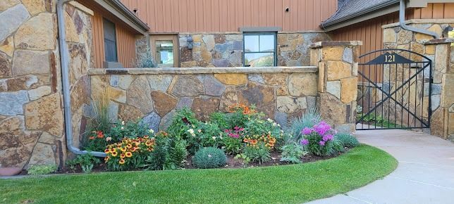 A stone wall with a gate and flowers in front of a house.
