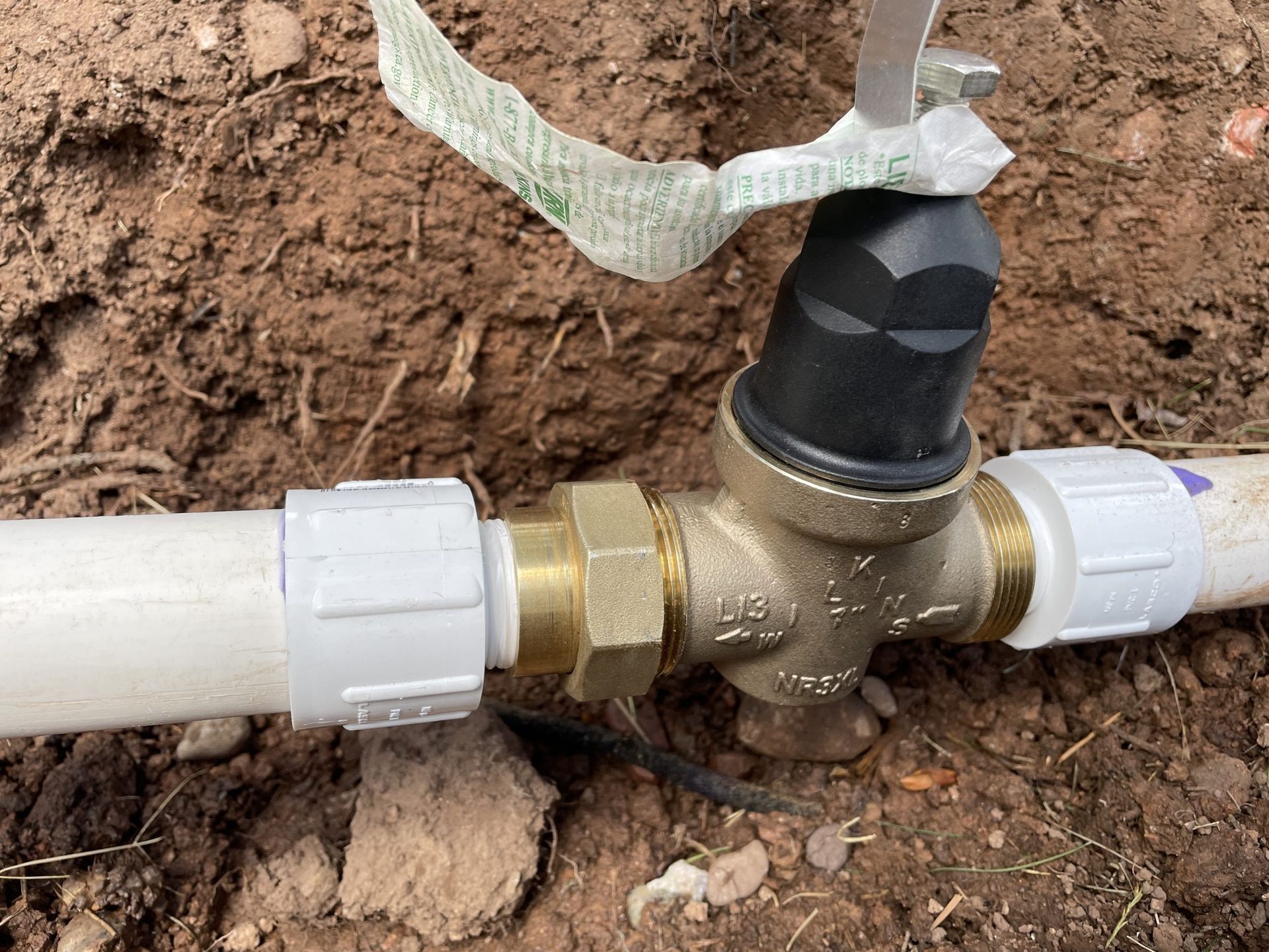 A close up of a water valve on a pipe in the dirt.