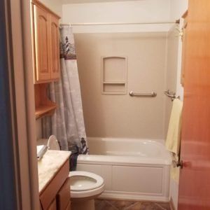 A bathroom with a toilet , tub , shower and cabinets.
