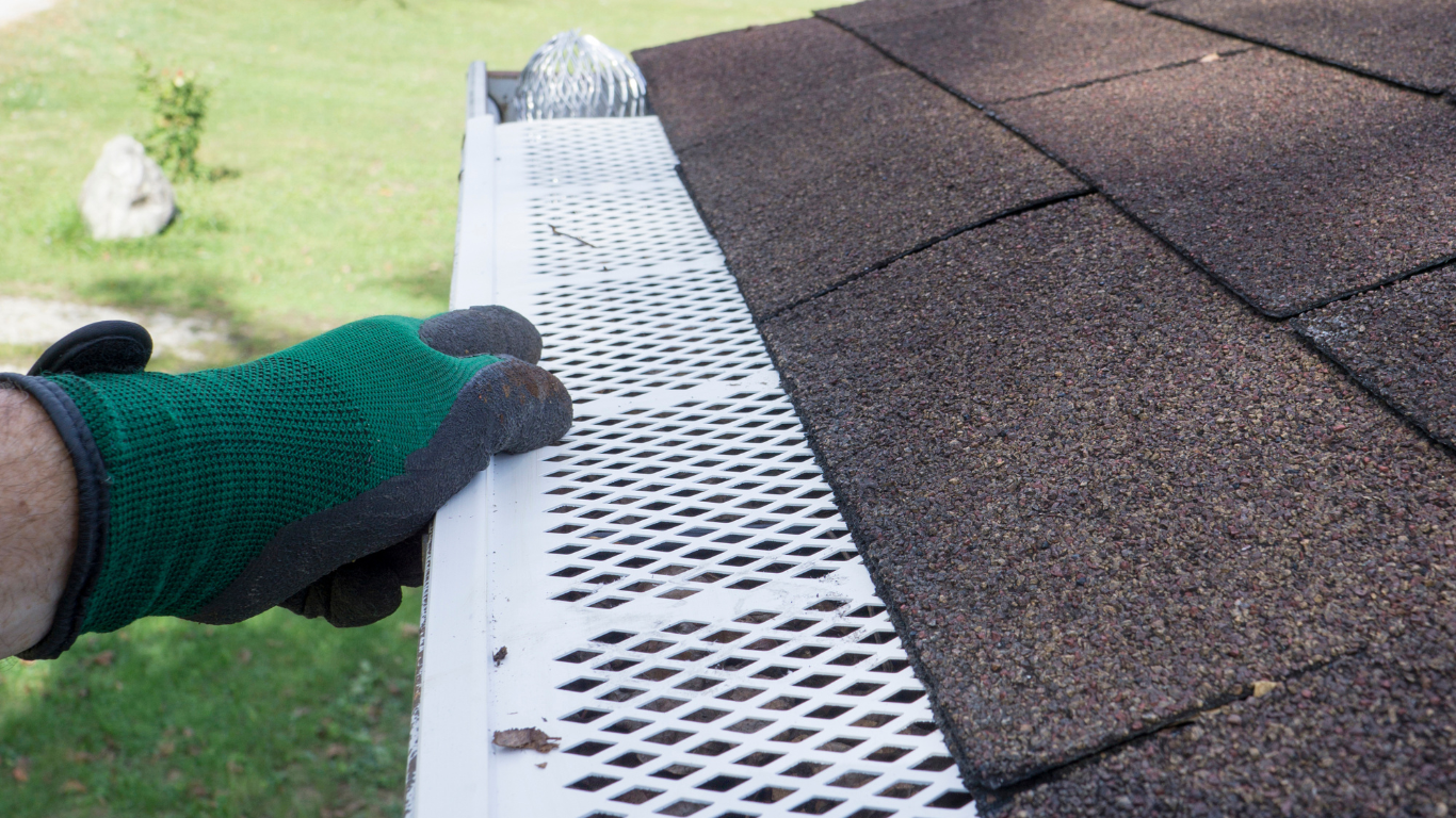 A person wearing gloves is cleaning a gutter on a roof.
