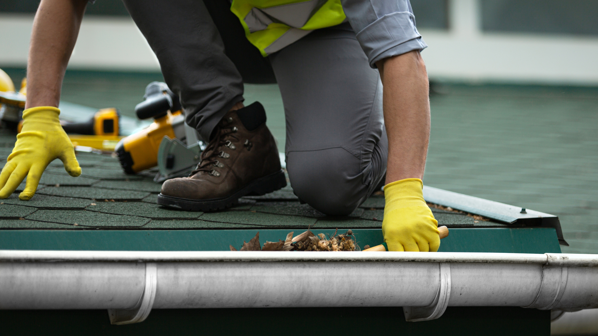 A man wearing yellow gloves is cleaning a gutter on a roof.