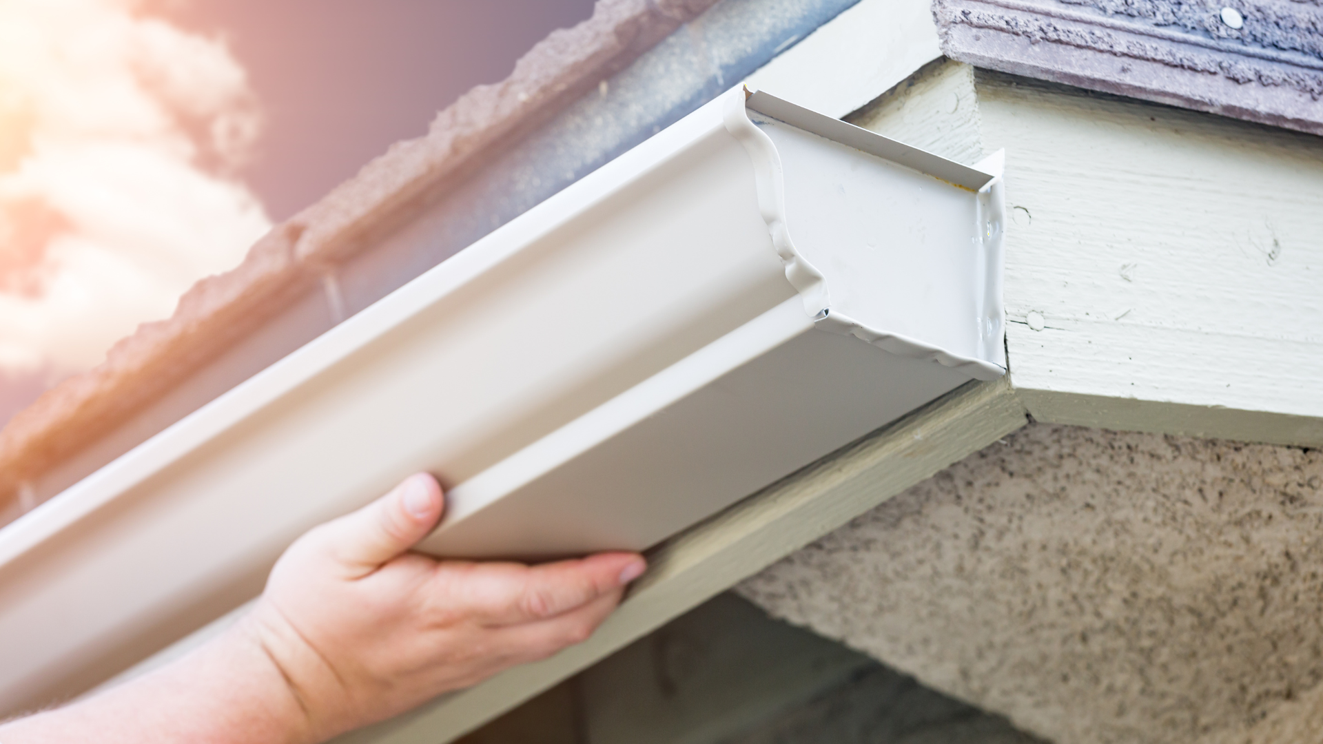 A person is installing a gutter on the side of a building.