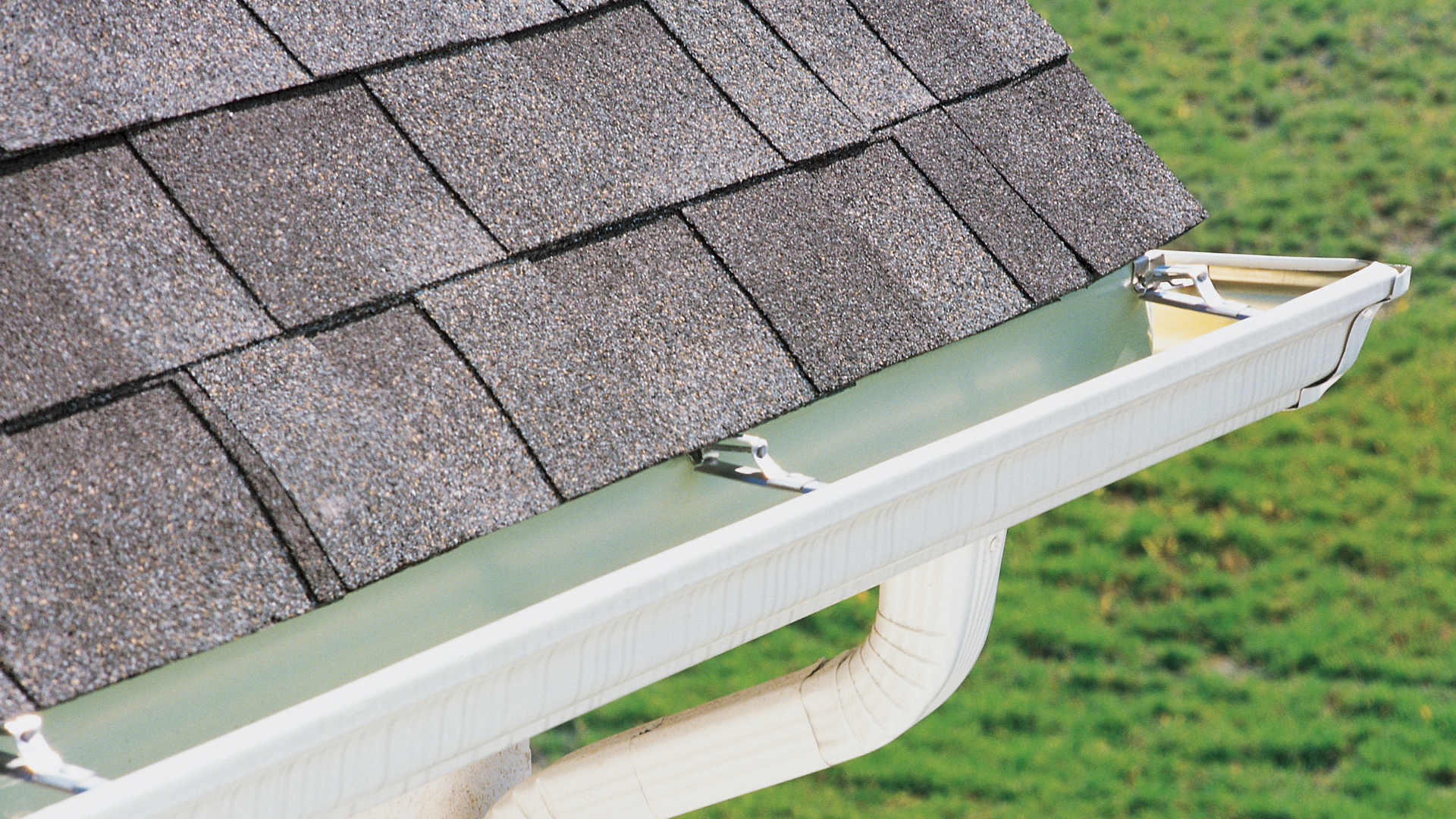 A white gutter is attached to the roof of a house.