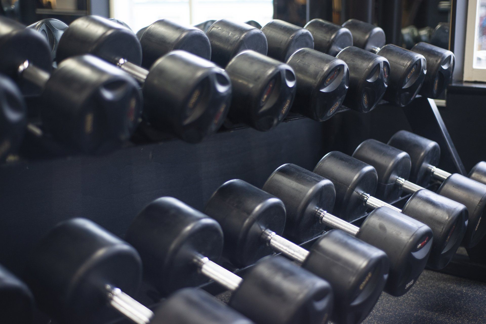 Een rij zwarte halters staat opgesteld op een rek in een sportschool.