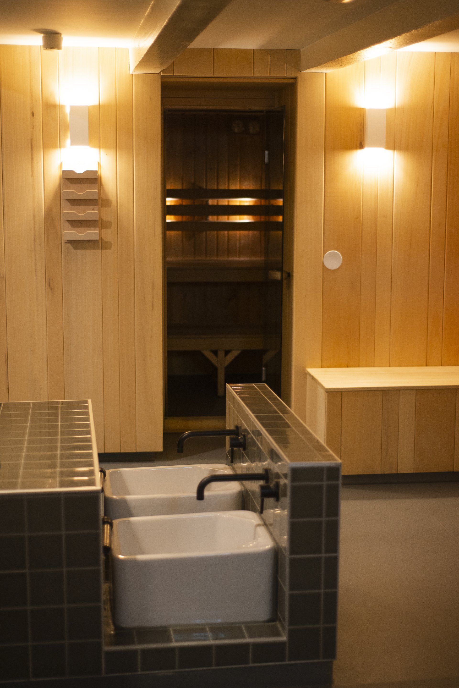 Een badkamer met twee wastafels en een sauna op de achtergrond