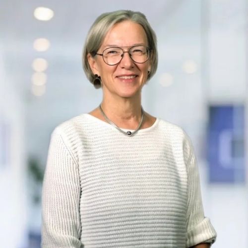 A woman wearing glasses and a white sweater is smiling for the camera.