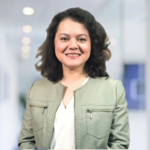 A woman in a green jacket and white shirt is smiling for the camera.