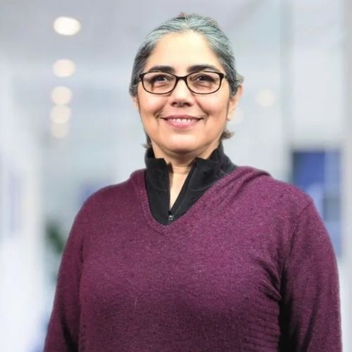 A woman wearing glasses and a purple sweater is smiling for the camera.