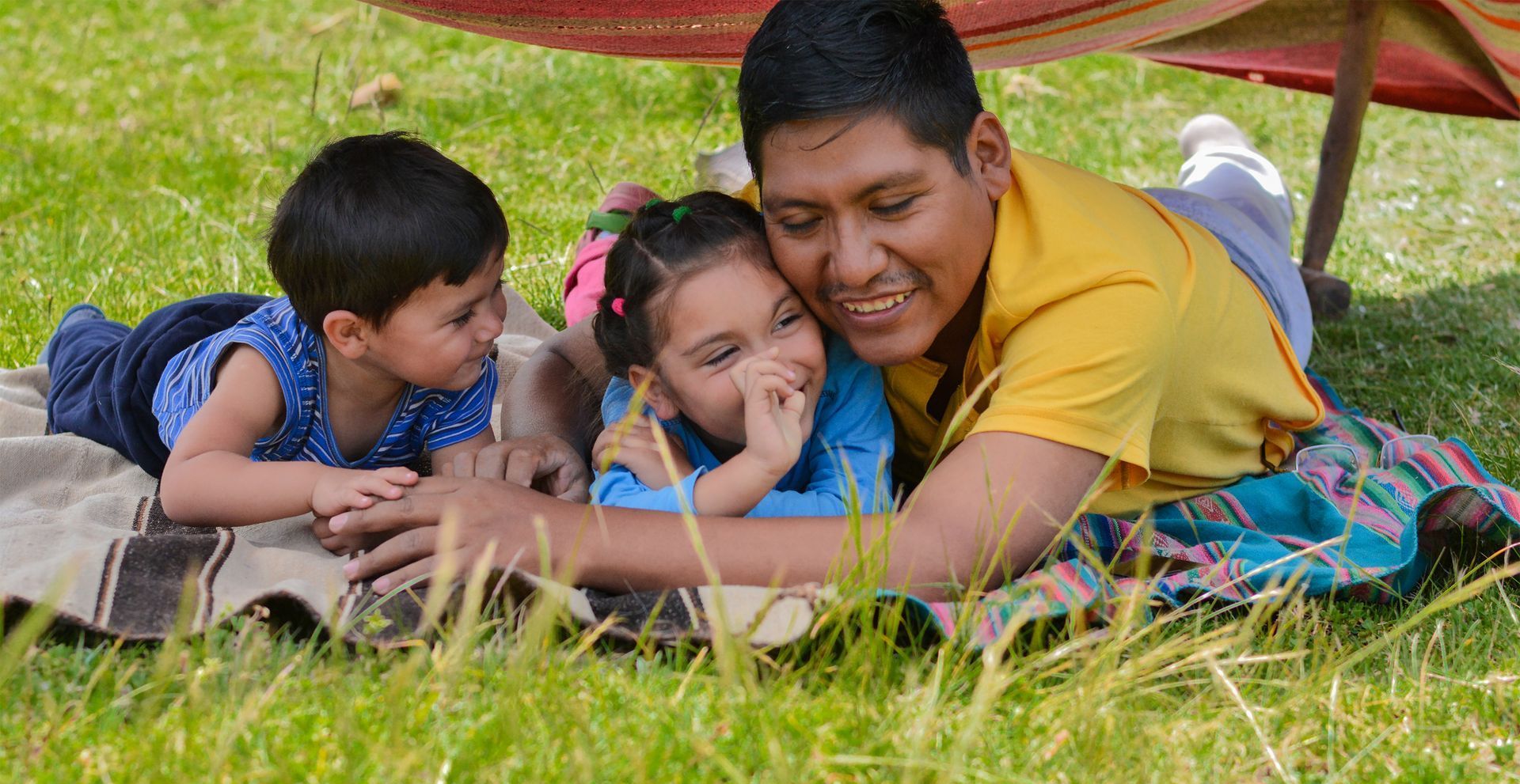 A man and two children are laying on a blanket in the grass.