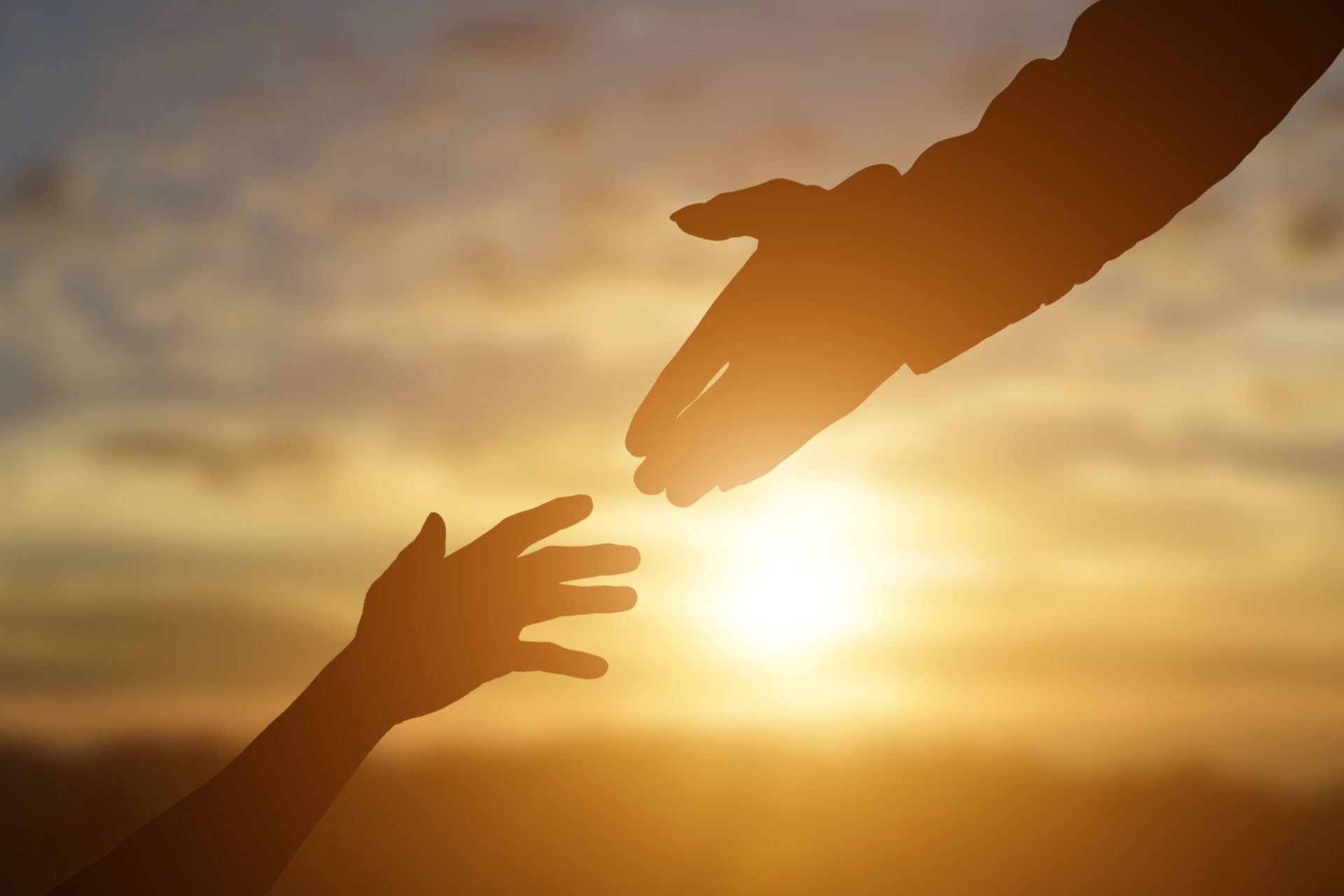 A person is reaching out to help another person at sunset.