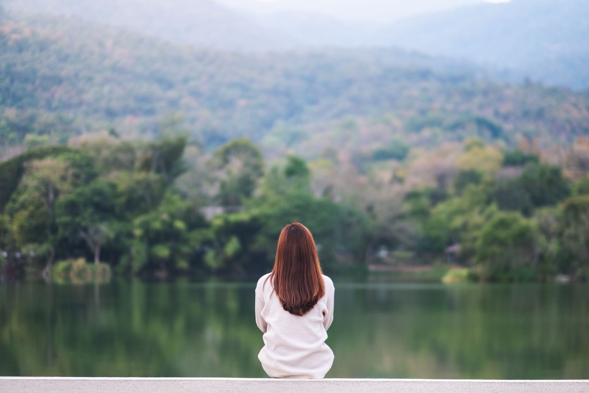 A woman is sitting on a ledge overlooking a lake.