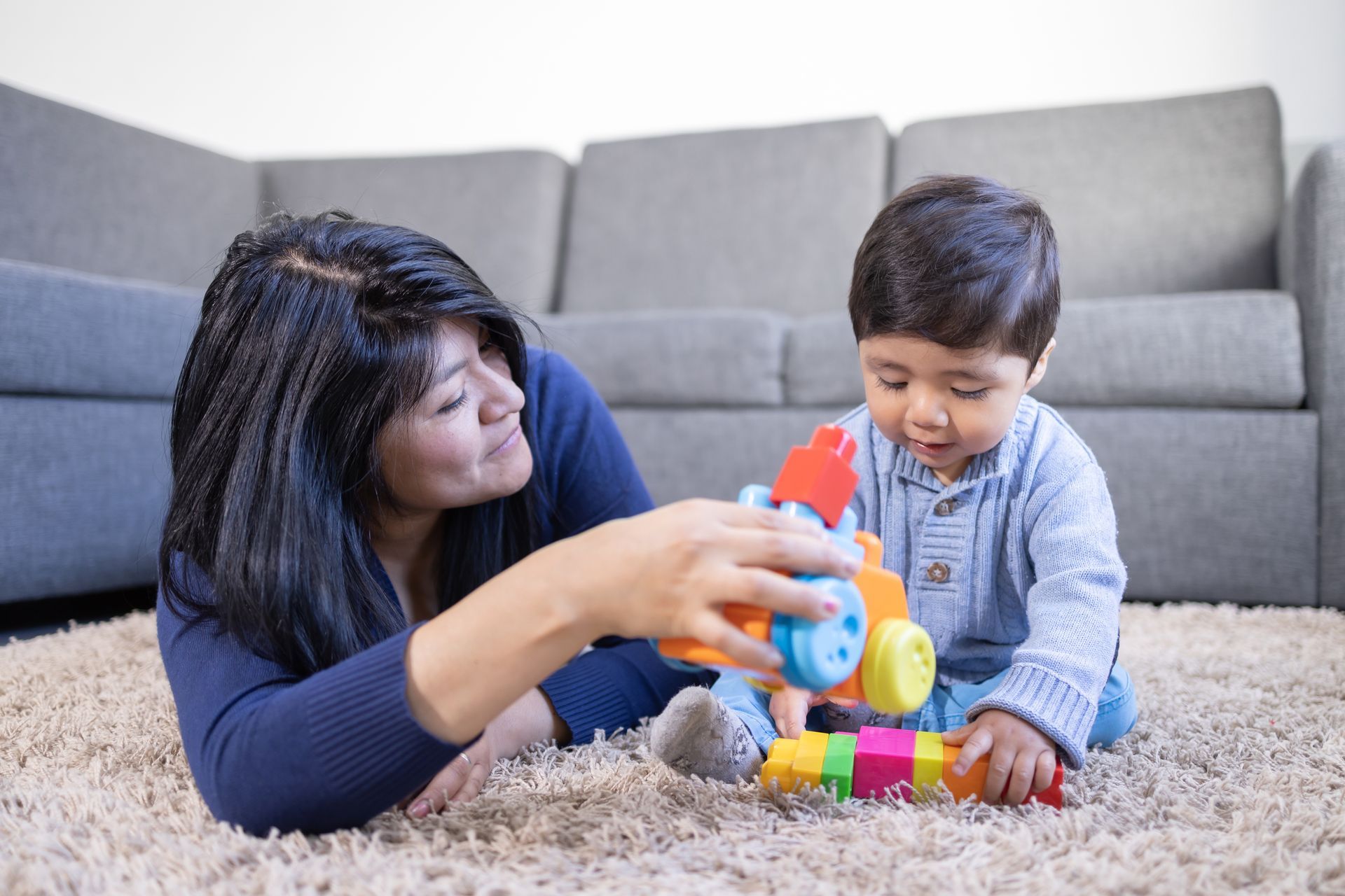 A woman and a baby are playing with toys on the floor.